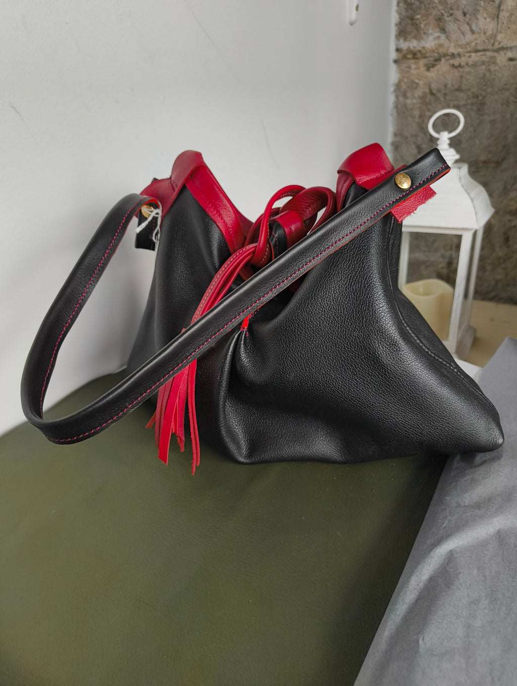 sac en cuir de veau noir et rouge avec une bandoulière à porter  à l' épaule et une lanière en pompon pour fermeture 
